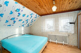 Podkrovní ložnice s dřevěným stropem a parketovou podlahou, vybavená velkými okny a dekorativní tapetou pro světlý a útulný vzhled.