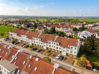 Letecký pohled na moderní řadové domy s červenou střechou v klidné rezidenční čtvrti, okolní zeleň a parkovací místa před domy