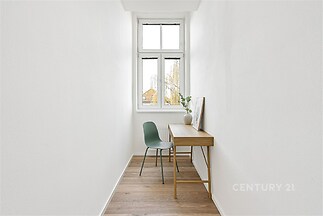 Úzká pracovná místnost s dřevěnou podlahou, moderním psacím stolem a velkým oknem poskytujícím dostatek světla.