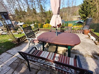 Terasa s venkovním posezením, obklopená zelení, dlažba a výhled do přírody, ideální pro relaxaci nebo rodinné setkání.