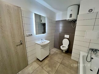 Moderní koupelna s dlažbou, světlým obkladem a vanou. Vestavěný bojler poskytuje efektivní ohřev vody. Vhodná kombinace barev a prvků.