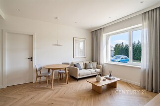 Světlý obývací pokoj s parketovou podlahou, velká okna a moderní nábytek, světlý interiér s minimalistickým stylem.