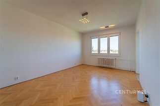 Světlý obývací pokoj s parketovou podlahou, velkými okny a bílými stěnami, moderní osvětlení, ideální prostor pro rodinné bydlení.