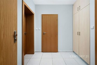 Předsíň s dlažbou, světlými vestavěnými skříněmi a dřevěnými dveřmi nabízí moderní úložné řešení a čistý design.