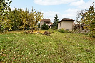 Prostorná zahrada s udržovaným trávníkem, obklopená stromy a keři, ideální pro rodinné aktivity, nabízí soukromí a klid v přírodní scenérii.