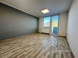 Světlý obývací pokoj s laminátovou podlahou, velká okna a moderní úprava stěn nabízí prostor pro pohodlné bydlení v rekonstruovaném bytě.