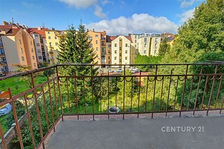 Balkon s kovovým zábradlím nabízí výhled na klidné zástavbě s parkem. Ideální pro relaxaci, obklopený zelení a slunečním světlem.