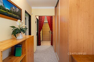 Úzká chodba s vestavěnými skříněmi, dřevěnými prvky a kobercem, světlé stěny, vchod do dalších místností, moderní interiér