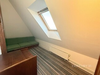 Podkrovní pokoj s kobercem a střešním oknem, který zajišťuje dostatek světla. Stěny jsou světlé, nábytek dřevěný.
