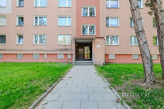 Vstup bytového domu s udržovaným trávníkem, moderní fasádou a plastovými okny v klidné lokalitě.