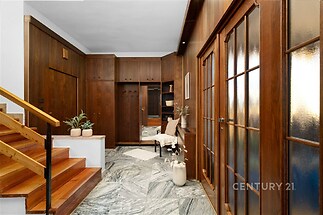 Předsíň s dřevěným obložením, mramorová dlažba, vestavěné skříně, klasický styl, široké schody, elegantní dřevěné dveře, světlá atmosféra.
