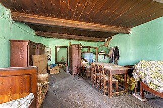 Jednoduchý obývací pokoj s dřevěným stropem, starožitným nábytkem a dřevěnými podlahami, vyžaduje rekonstrukci pro moderní bydlení.