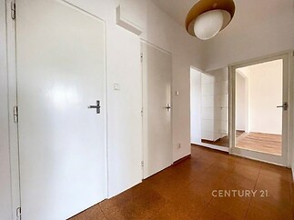 Chodba s parketovou podlahou, bílé stěny, moderní osvětlení, světlá dispozice, dveře vedoucí do dalších místností.