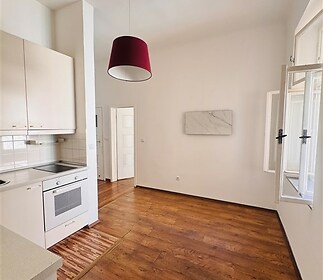 Kuchyňský kout s dřevěnou podlahou, světlými skříňkami a velkým oknem, moderní spotřebiče zajišťují pohodlí a útulnost.