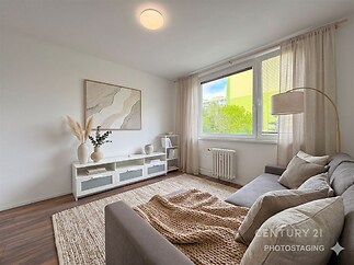 Světlý obývací pokoj s parketovou podlahou, velkým oknem a moderním nábytkem vytváří útulný a stylový interiér pro relaxaci.