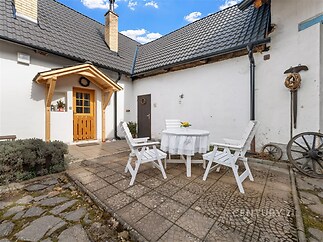 Venkovní terasa s dlažbou, dřevěným přístřeškem a rustikálním nábytkem, ideální pro relaxaci.