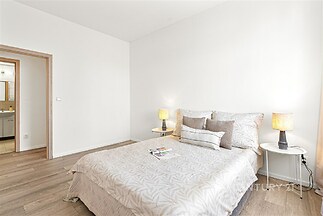 Světla ložnice, parketová podlaha, moderní design, vkusně zařízená, světlé stěny, pohodlné lůžko, útulná atmosféra, elegantní osvětlení.