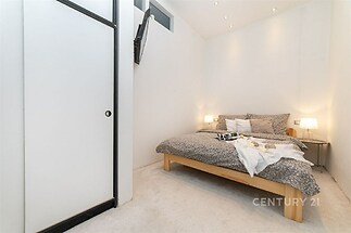 Světlá ložnice s moderním designem, vestavěné skříně, světlý koberec a minimalistické osvětlení vytváří útulnou atmosféru.