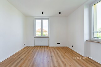 Světlý obývací pokoj s parketovou podlahou má velká okna a moderní osvětlení, ideální pro světlý a vzdušný interiér.