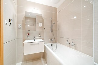 Moderní koupelna s elegantní dlažbou, bílou sanitou a zrcadlovou skříňkou. Prostor je světlý a udržovaný, vhodný pro pohodlné bydlení.
