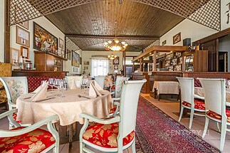 Stylová restaurace s dřevěným stropem, dekorativními lustry a kobercem. Kombinace dřevěného nábytku a textilních detailů vytváří útulnou atmosféru.