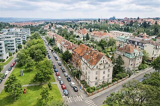 Letecký pohled na činžovní domy s červenými střechami v rezidenční části města, okolní zeleň a moderní budovy vytvářejí atraktivní lokalitu.