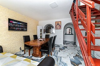 Jídelní kout s mramorovou dlažbou, dekorativní kamennou stěnou a dřevěným stolem. Kovové schody vedou do patra, vytváří moderní atmosféru.