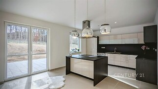 Moderní kuchyň s keramickou dlažbou, velká okna zajišťují dostatek světla, elegantní závěsná svítidla dominují prostoru.