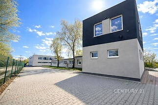 Průmyslová budova s moderní fasádou a dlážděným parkovištěm, oplocené prostory, kvalitní zázemí v blízkosti přírody.