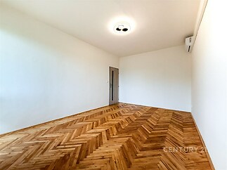 Prázdný pokoj s parketovou podlahou, bílými stěnami a moderní klimatizací nabízí světlý a čistý prostor ideální pro osobní úpravy.