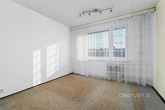 Světlý obývací pokoj s velkými okny, koberec na podlaze a moderní osvětlení, ideální pro rekonstrukci dle vlastního stylu.