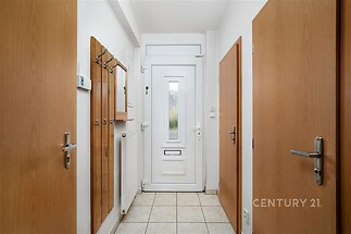 Vstupní hala s dlažbou, bílými stěnami a dřevěnými dveřmi, vybavená praktickým věšákem a zrcadlem, poskytuje moderní a světlý prostor.