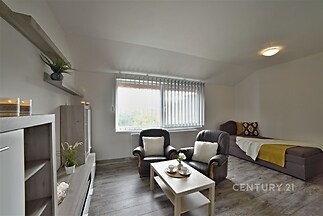 Světle zařízený obývací pokoj s parketovou podlahou, velkými okny a moderním nábytkem, nabízí útulný a světlý prostor k relaxaci.