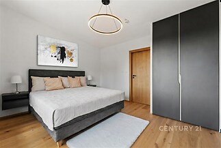 Moderní ložnice s parketovou podlahou, vestavěné skříně a minimalistické osvětlení, nabízí komfortní a stylové prostředí pro relaxaci.