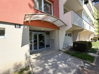 Vstupní prostor bytového domu s moderním přístřeškem a dlažbou, dobře udržovaný exteriér, vhodný pro rezidenční účely.