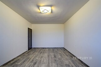 Prázdný pokoj s moderními šedými podlahami, bílými stěnami a minimalistickým stropním osvětlením, vhodný pro adaptaci.