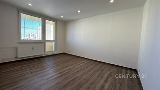 Světlý obývací pokoj s parketovou podlahou, velká okna poskytují dostatek přirozeného světla, moderní bílá výmalba.