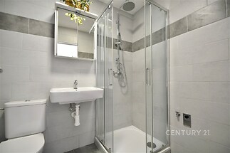 Moderní koupelna s dlažbou a sprchovým koutem, světlé obklady a závěsné umyvadlo, čistý a renovovaný styl.