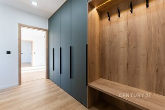 Vstupní chodba s moderními vestavěnými skříněmi, dřevěnými obklady a parketovou podlahou, poskytující světlý a elegantní vzhled.