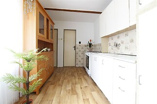 Světlá kuchyň s parketovou podlahou, vestavěnými skříněmi a rustikálním obkladem na stěnách, působí útulně a vzdušně.