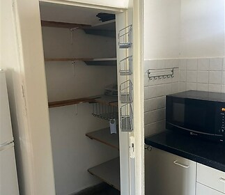 Praktická spíž s policemi, dlažbou a bílými stěnami, přiléhající k moderní kuchyni s mikrovlnnou troubou a úložným prostorem.
