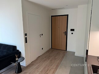 Vstupní hala s moderní dlažbou, dřevěnými dveřmi a světlou výmalbou, navazující na parketovou podlahu obývacího pokoje.