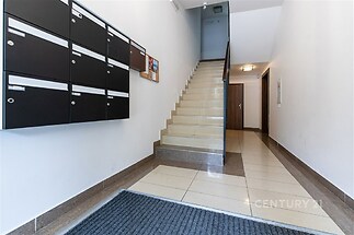 Vstupní hala s keramickou dlažbou, moderními schody a poštovními schránkami. Světlé stěny vytvářejí elegantní a čistý prostor.