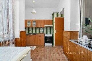 Kuchyň s dřevěnými skříňkami, parketovou podlahou a retro obkladem zelené barvy, vybavená plynovým sporákem a velkým oknem.