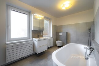 Prostorná koupelna s moderní dlažbou, velkými okny a novým osvětlením nabízí elegantní a světlý prostor k relaxaci.