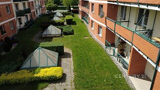 Balkóny bytového domu s cihlovou fasádou a zeleným travnatým dvorem. Velká okna a moderní konstrukce nabízí světlé prostory.