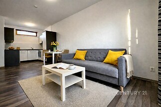 Světlý obývací pokoj s moderní sedačkou, parketovou podlahou a velkými okny, propojený s kuchyní v elegantním stylu.