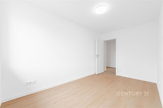 Prázdná místnost s dřevěnou podlahou, světlými stěnami a moderním osvětlením, ideální pro personalizaci a variabilní interiérový design.