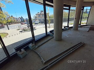 Prázdný komerční prostor s velkými okny a betonovou podlahou, ideální pro kancelář. Otevřený půdorys a neutrální design nabízí flexibilitu.