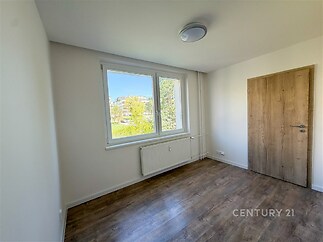 Světlá ložnice s velkými okny, dřevěnou podlahou a moderními dveřmi, nabízí rekonstrukci a klidný výhled do zeleně